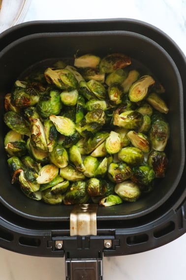 brussels sprouts in an air fryer basket near a sauce.