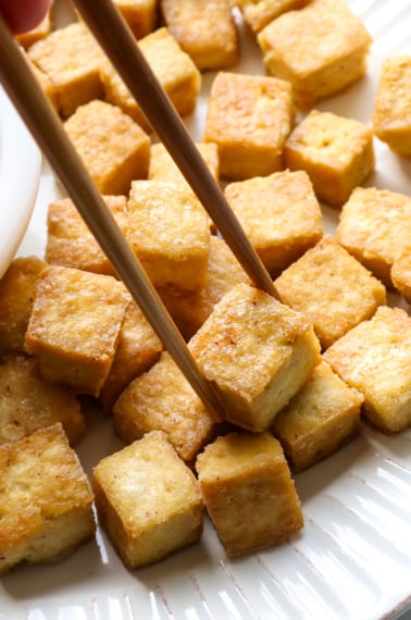 baked tofu pieces on a white plate with chopsticks.