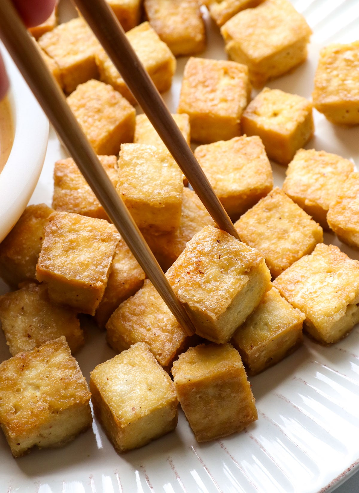 baked tofu pieces on a white plate with chopsticks.