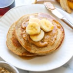 banana oatmeal pancakes stacked on a plate with peanut butter and banana.
