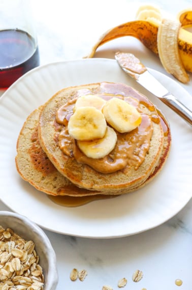 banana oatmeal pancakes stacked on a plate with peanut butter and banana.
