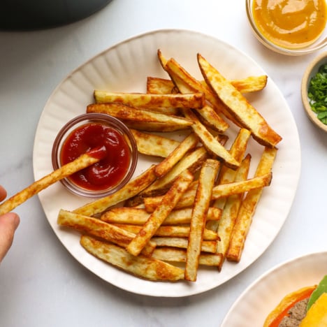 french fry dipped into ketchup on a white plate.