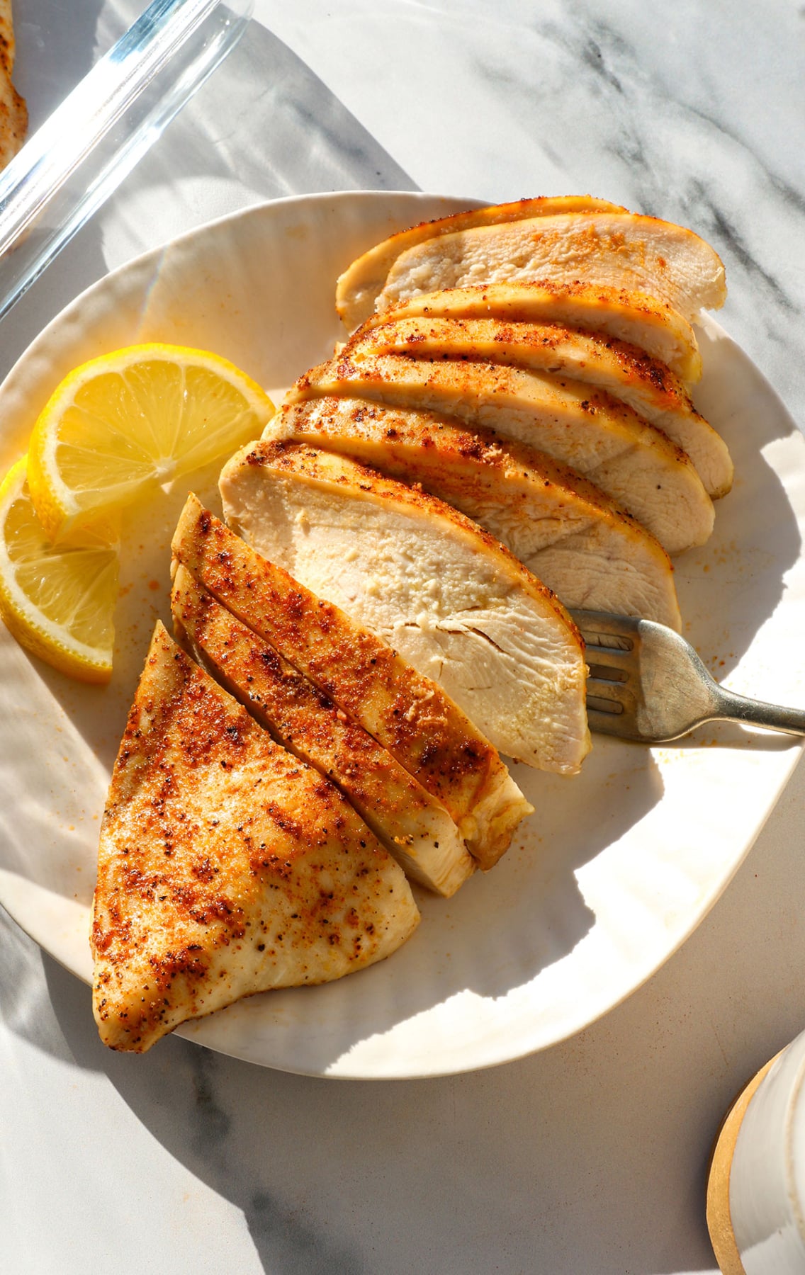 close-up of sliced oven baked chicken breast on a white plate with lemon slices.