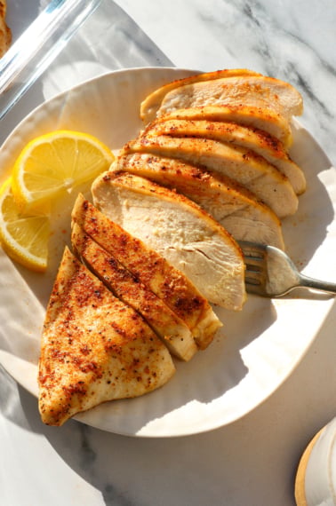 close-up of sliced oven baked chicken breast on a white plate with lemon slices.