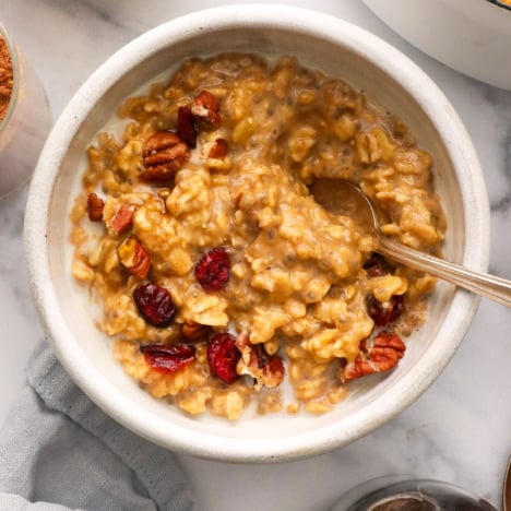 pumpkin oatmeal stirred with cranberries and pecans in a white bowl.