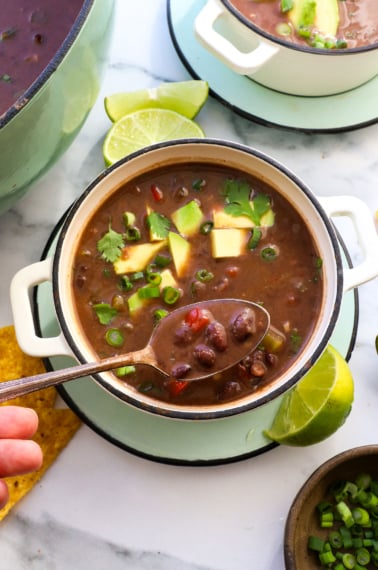 black bean soup lifted on a spoon over a white bowl.