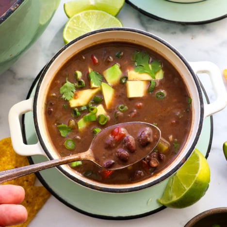 black bean soup lifted on a spoon over a white bowl.