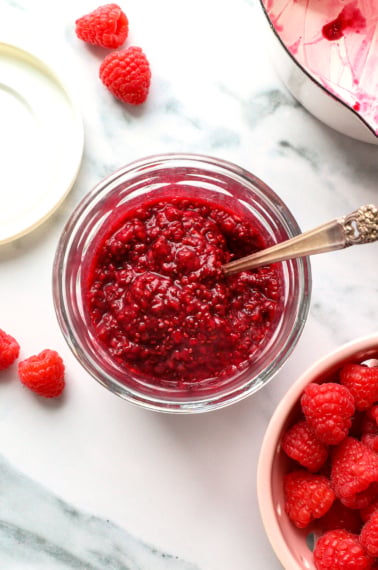 chia seed jam made with raspberries in a glass jar with a spoon.