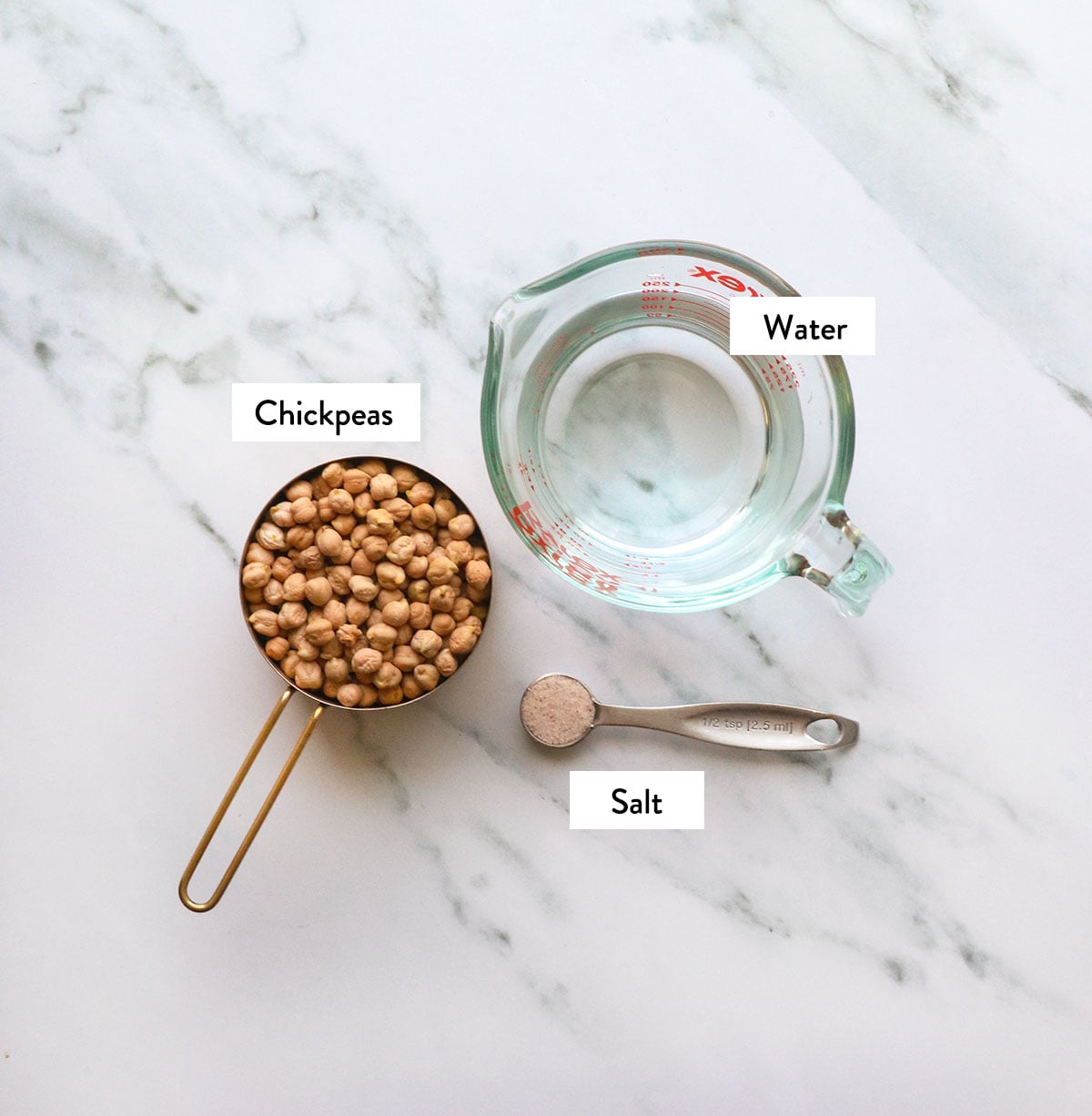 dried chickpeas, water, and salt labeled on a white surface.