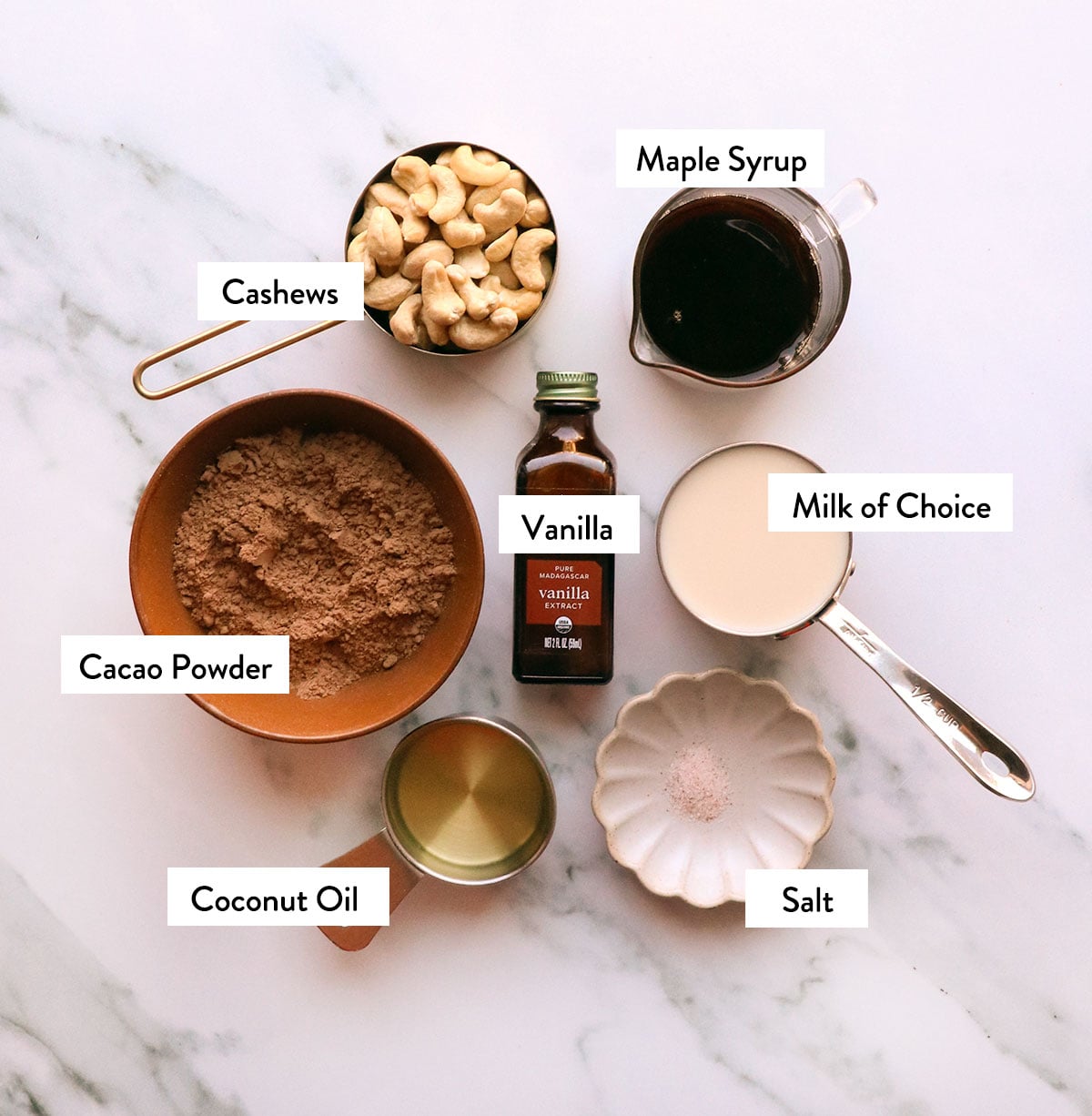 cashews, cacao powder, maple syrup, milk, and coconut oil labeled in bowls.