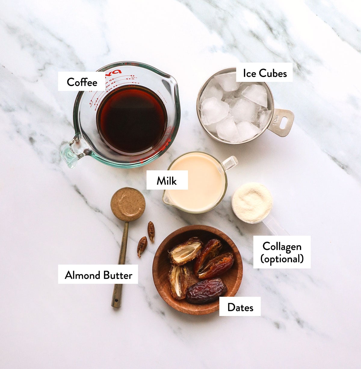 coffee, ice cubes, pitted dates, almond butter and milk labeled on a white surface.
