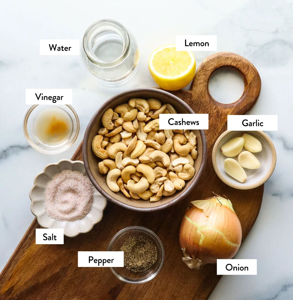 bowl of cashews, salt, pepper, lemon, garlic, and vinegar labeled on a cutting board.