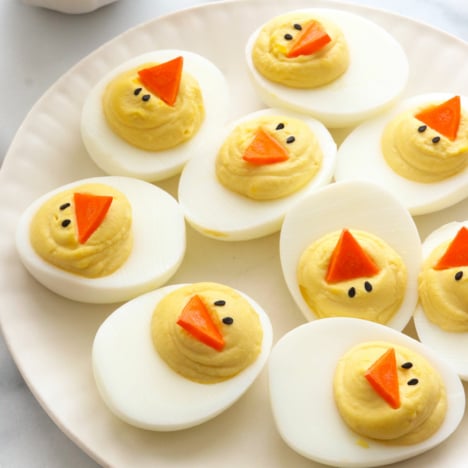 Easter deviled eggs topped with carrot beaks on a white plate.