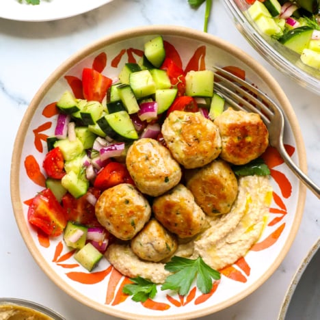 Greek chicken meatballs served in a bowl with hummus and cucumber salad.
