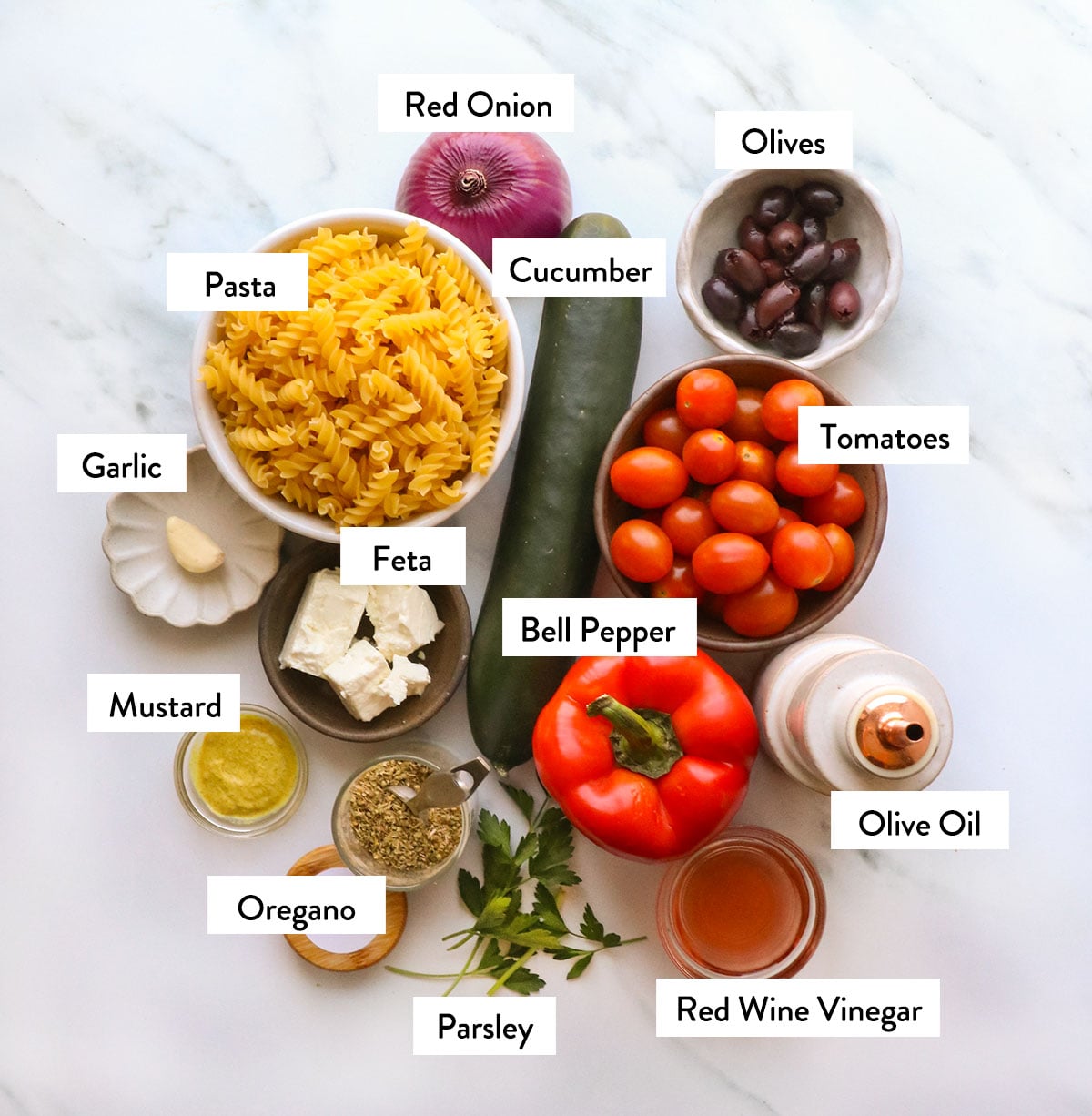 pasta, cucumber, tomatoes, olive oil, red onion, and garlic labeled in bowls.