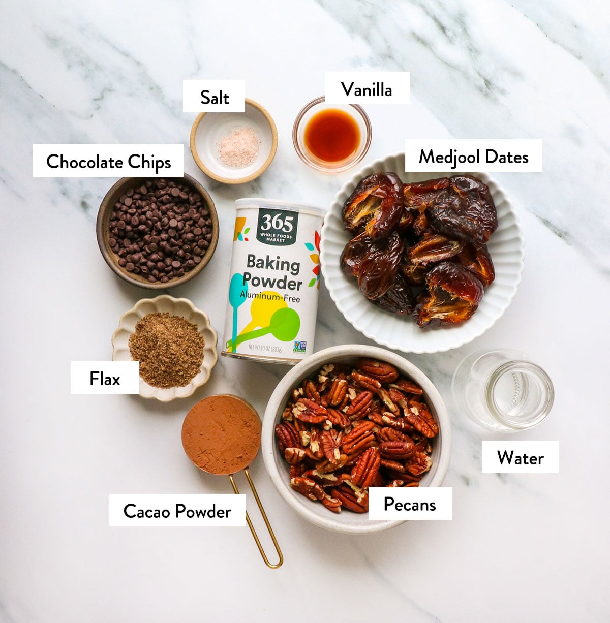 dates, pecans, baking powder, ground flax, and cacao powder labeled in bowls.