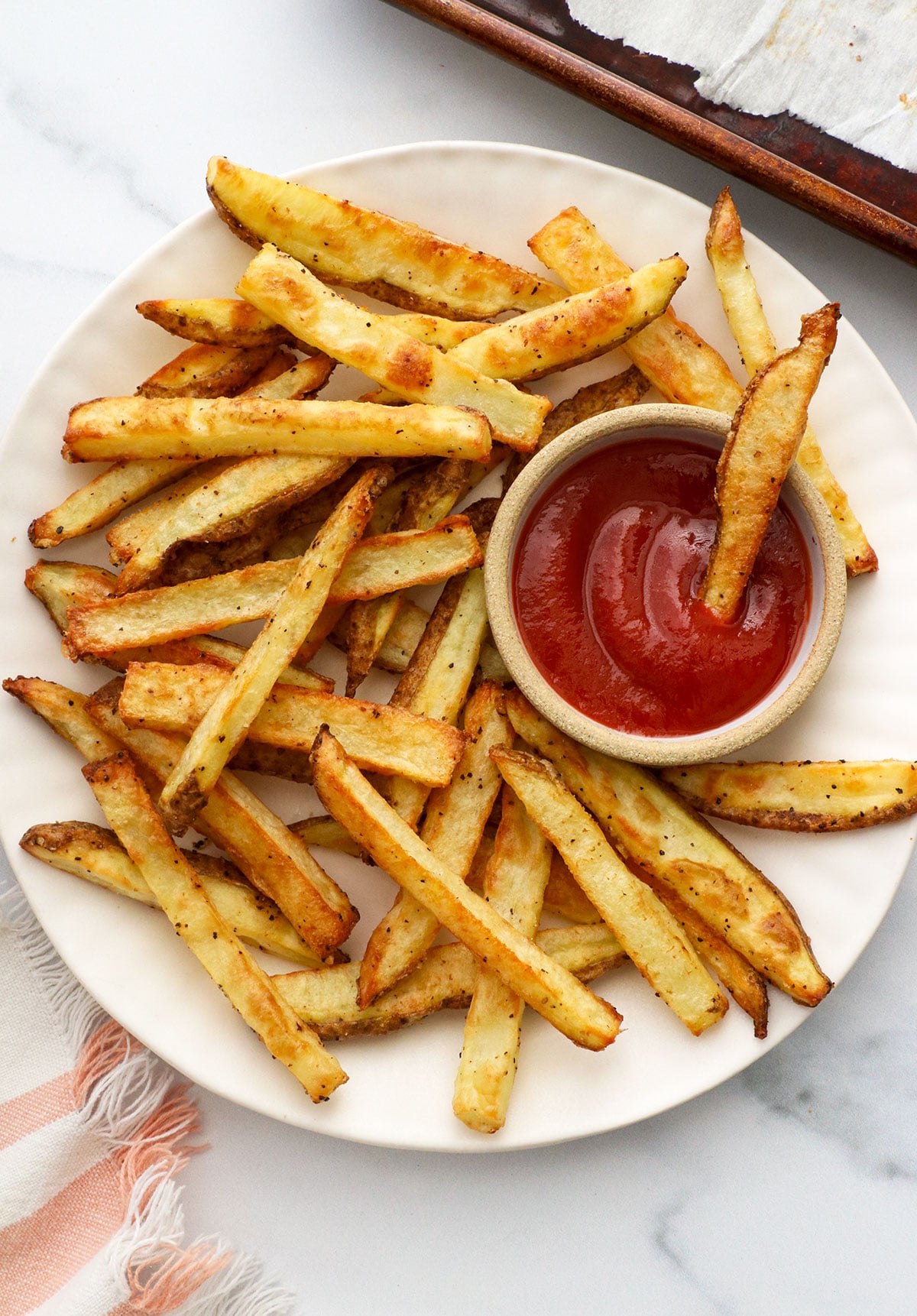 baked french fries served with ketchup on a plate.
