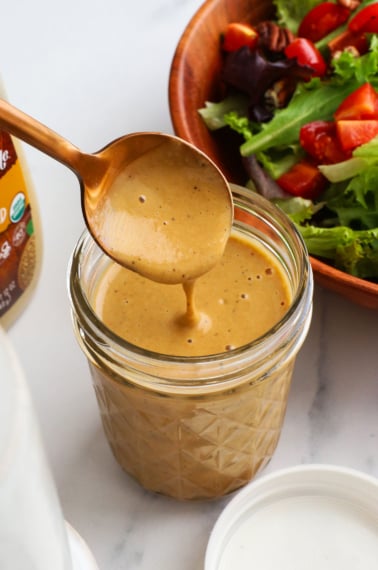 honey balsamic dressing poured off of a spoon into a jar.