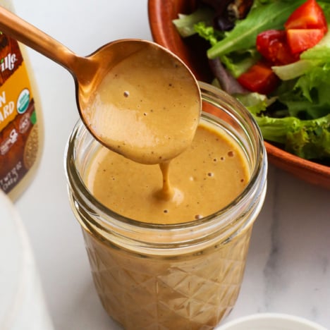 honey balsamic dressing poured off of a spoon into a jar.