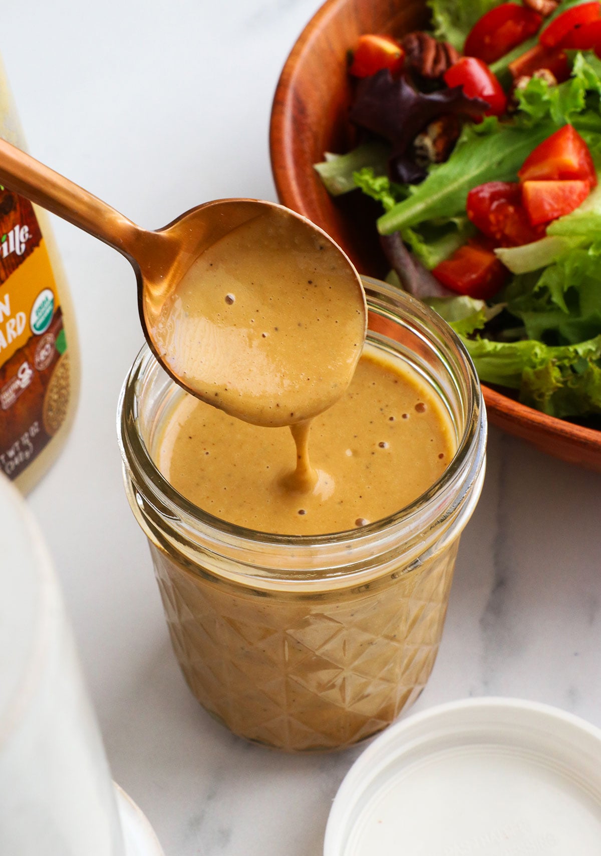 honey balsamic dressing poured off of a spoon into a jar.