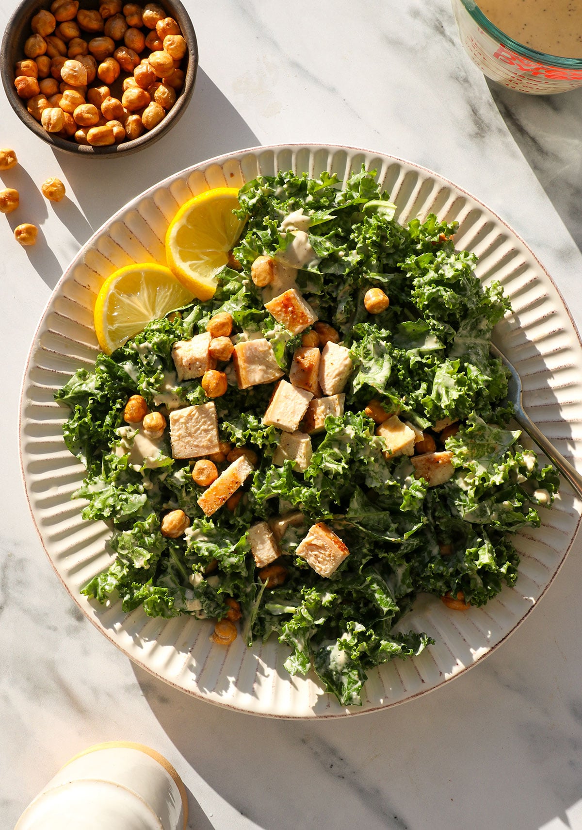 kale caesar salad topped with chicken and tahini dressing.