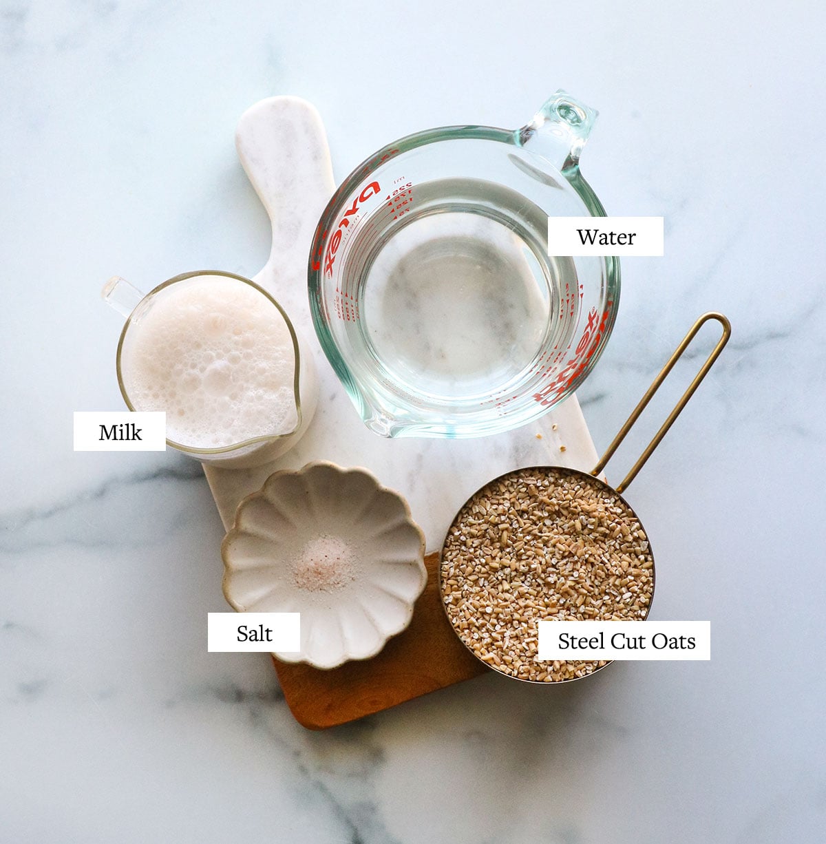 a cup of steel cut oats with water, milk, and salt on a marble board.
