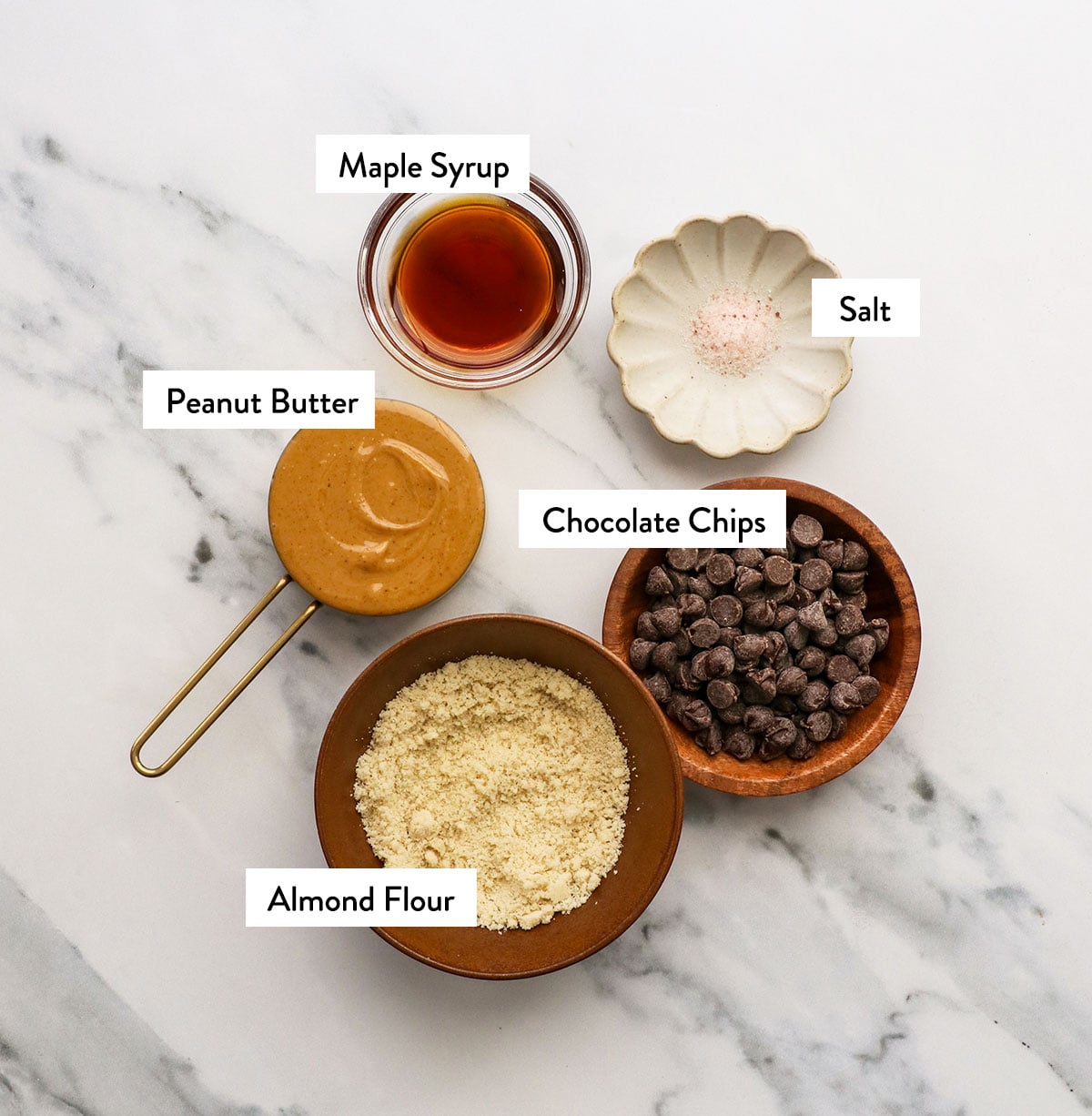 almond flour, peanut butter, maple syrup, chocolate chips, and salt in bowls with labels.