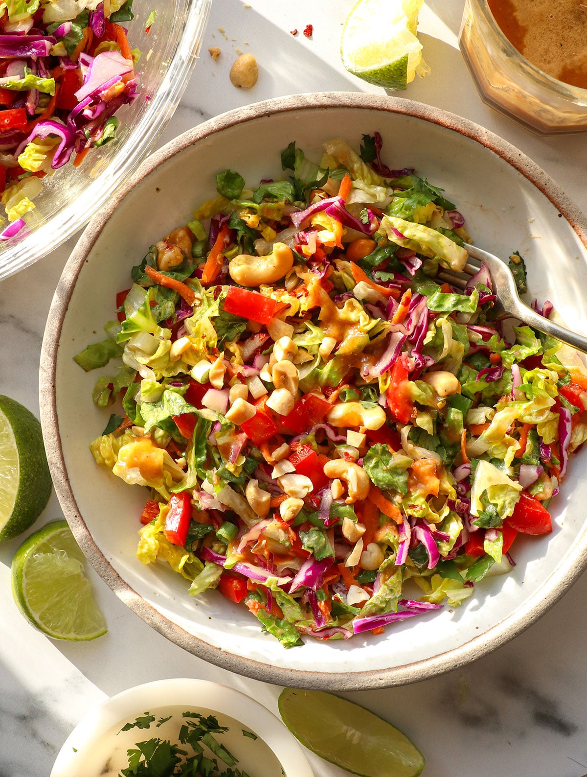 thai salad topped with peanut dressing in a white bowl with a fork.