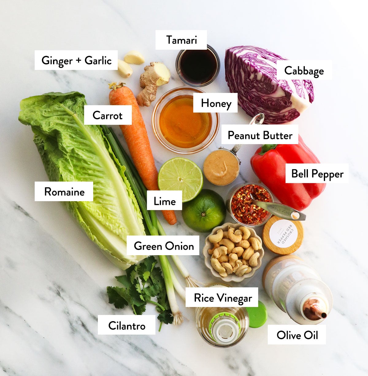 romaine lettuce, cabbage, carrots, peanut butter, cashews, bell pepper, and honey labeled on a white counter.