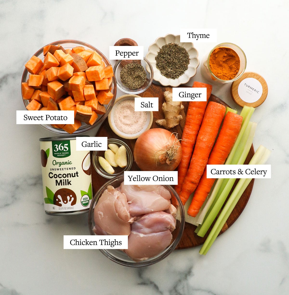 sweet potato cubes, chicken thighs, onion, carrots, celery, spices, and a can of coconut milk on a board.