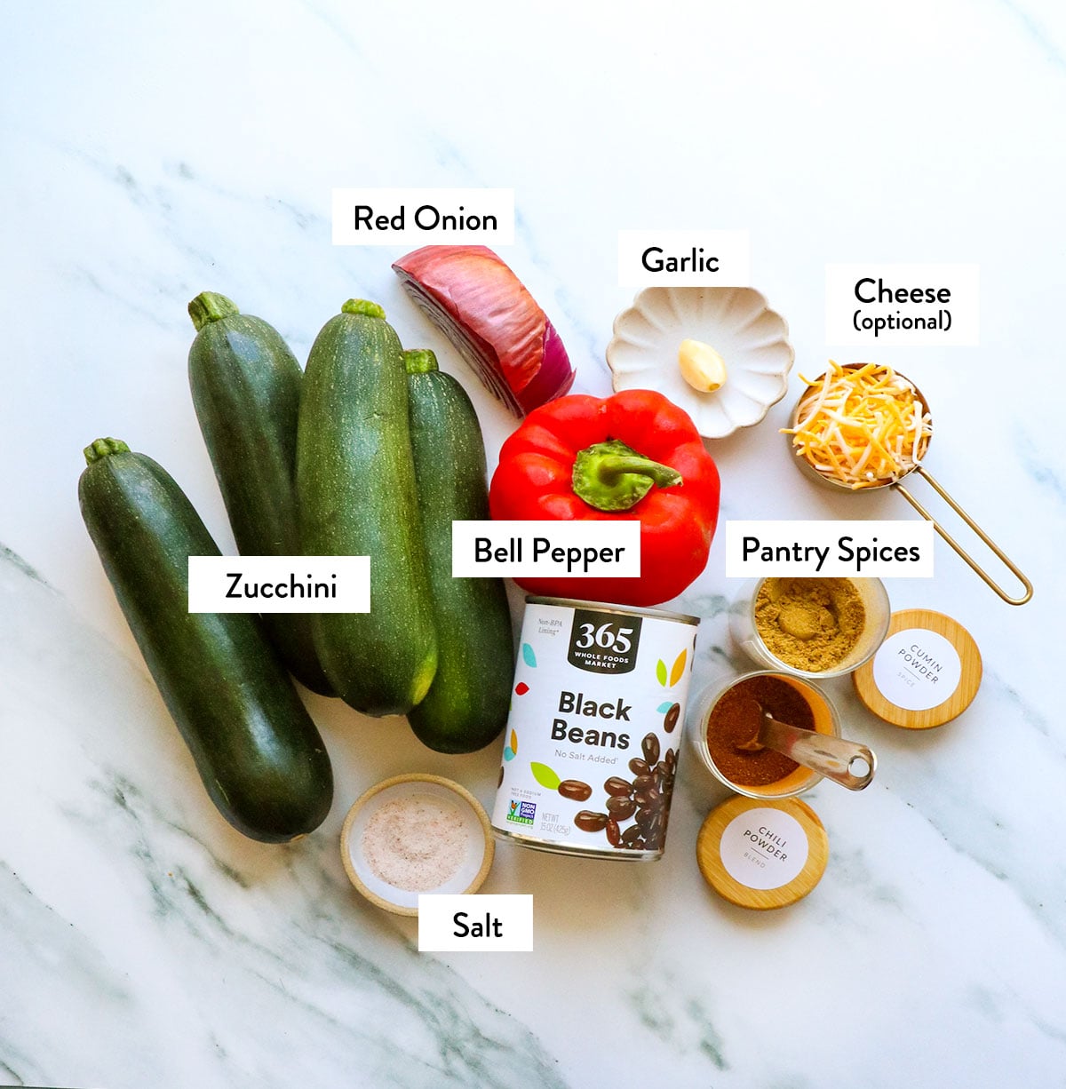zucchini, bell pepper, red onion, black beans, and spices labeled on a white surface. 