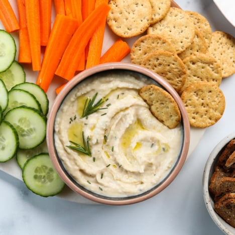 white bean dip topped with rosemary and served with crackers and sliced veggies.